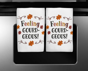 Waffle weave towels featuring “Feeling Gourdgeous” text with fall leaves in autumn colors, displayed on oven handle.